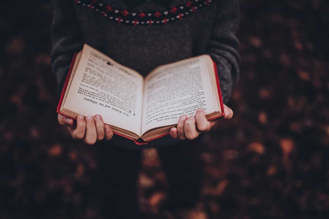 djevojka u puloveru čita knjigu crvenih korica.
