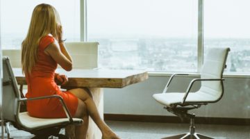 Žena u narančastoj haljini sjedi u uredu s pogledom na grad
