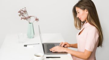 Žena u ružičastoj haljini sjedi pored laptopa