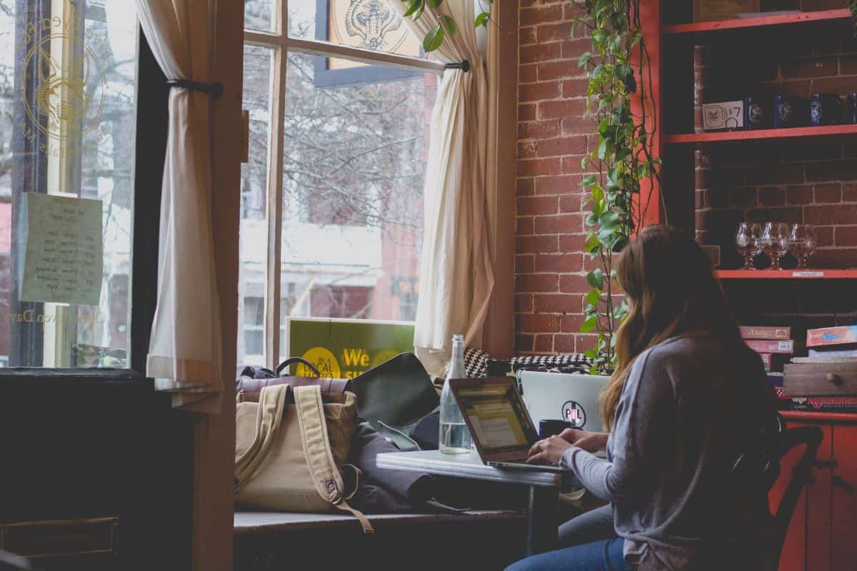 Žena sjedi za stolom u kafiću i radi na laptopu